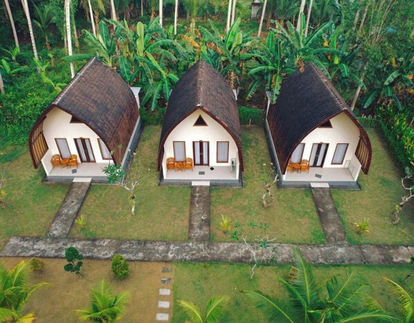 Three bungalow-style houses with thatched roofs, arranged in a row with a central pathway. Each house has a porch with seating and a small table. - The Dulu Penida Villa (Penida Island)