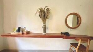 Um quarto com uma escrivaninha de madeira, uma cadeira, um vaso com plantas secas e um espelho redondo na parede.