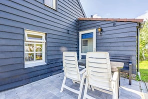 A patio with two white chairs and a table, a window, and a door with a blue awning.
