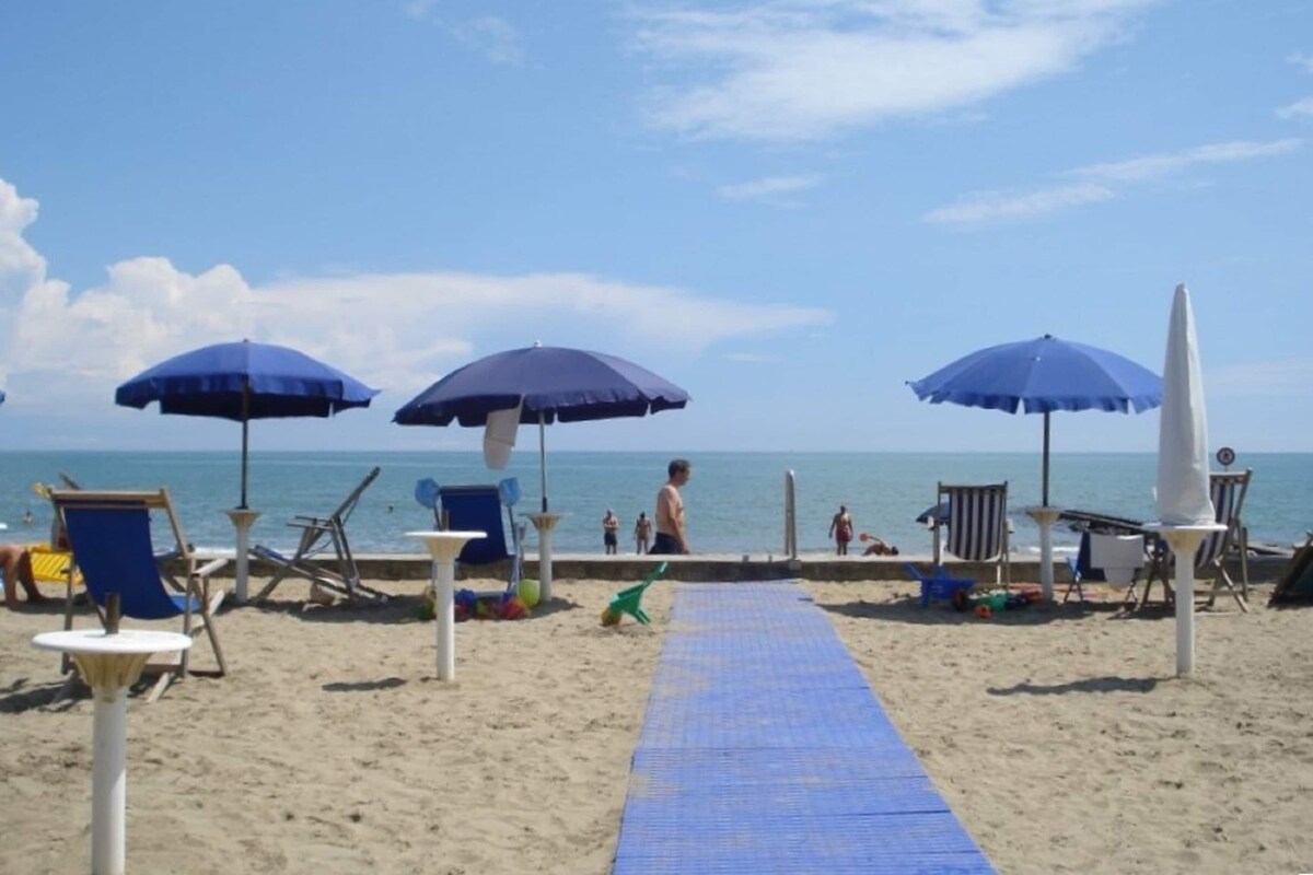 Une plage avec des parasols bleus, des chaises longues et un tapis bleu qui mène à l’eau.