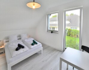 Un dormitorio con una cama, una mesa y un ventanal con vistas a una casa y vegetación.