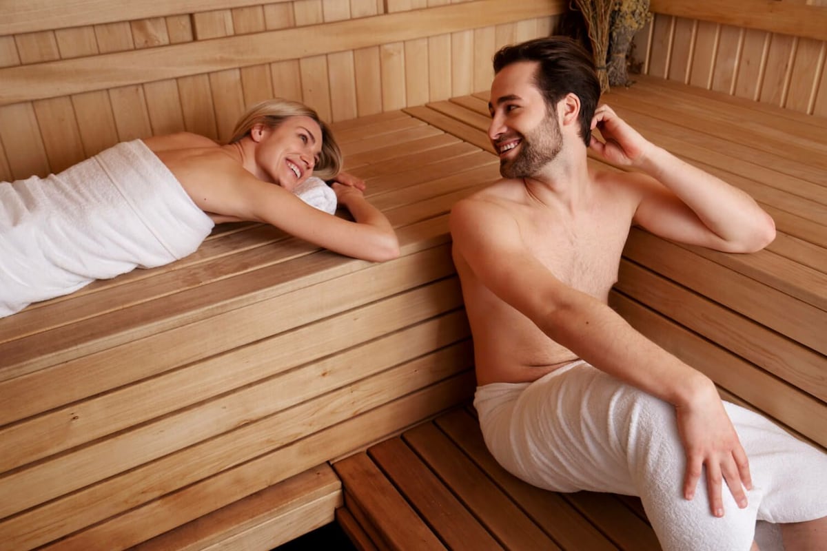 Two individuals in a sauna with wooden benches and benches.
