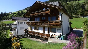 Un chalet à deux étages doté d’un balcon en bois, d’une antenne parabolique et d’un jardin fleuri.