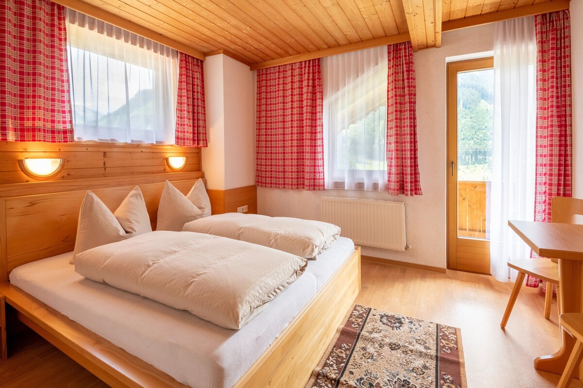 Una habitación con paneles de madera, una cama, dos mesitas de noche, un radiador y una ventana con cortinas.