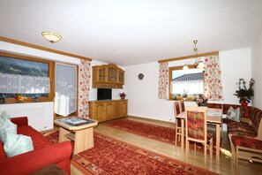 Una sala de estar acogedora con un sofá rojo, una mesa de comedor de madera y sillas. Se observa una zona de cocina con armarios de madera y un televisor.
