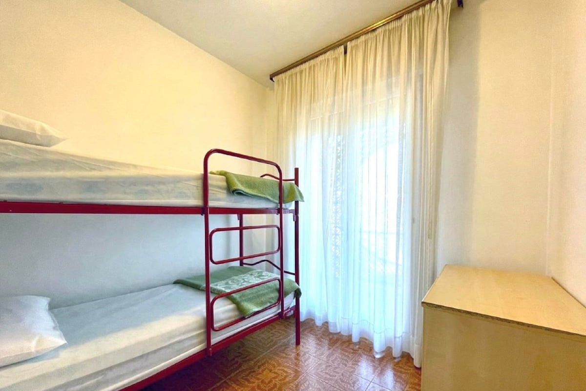 Een slaapkamer met stapelbed, raam, gordijnen en een lamp.
