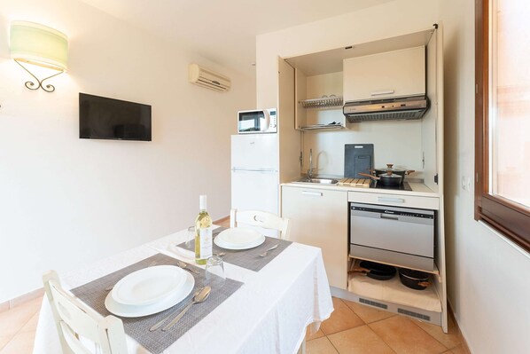 A compact kitchen with a microwave, oven, and sink, a dining table set with plates and cutlery, and a wall-mounted flat-screen TV. - Apartments With Shared Pool, Vignola/mare Aglientu (Aglientu)