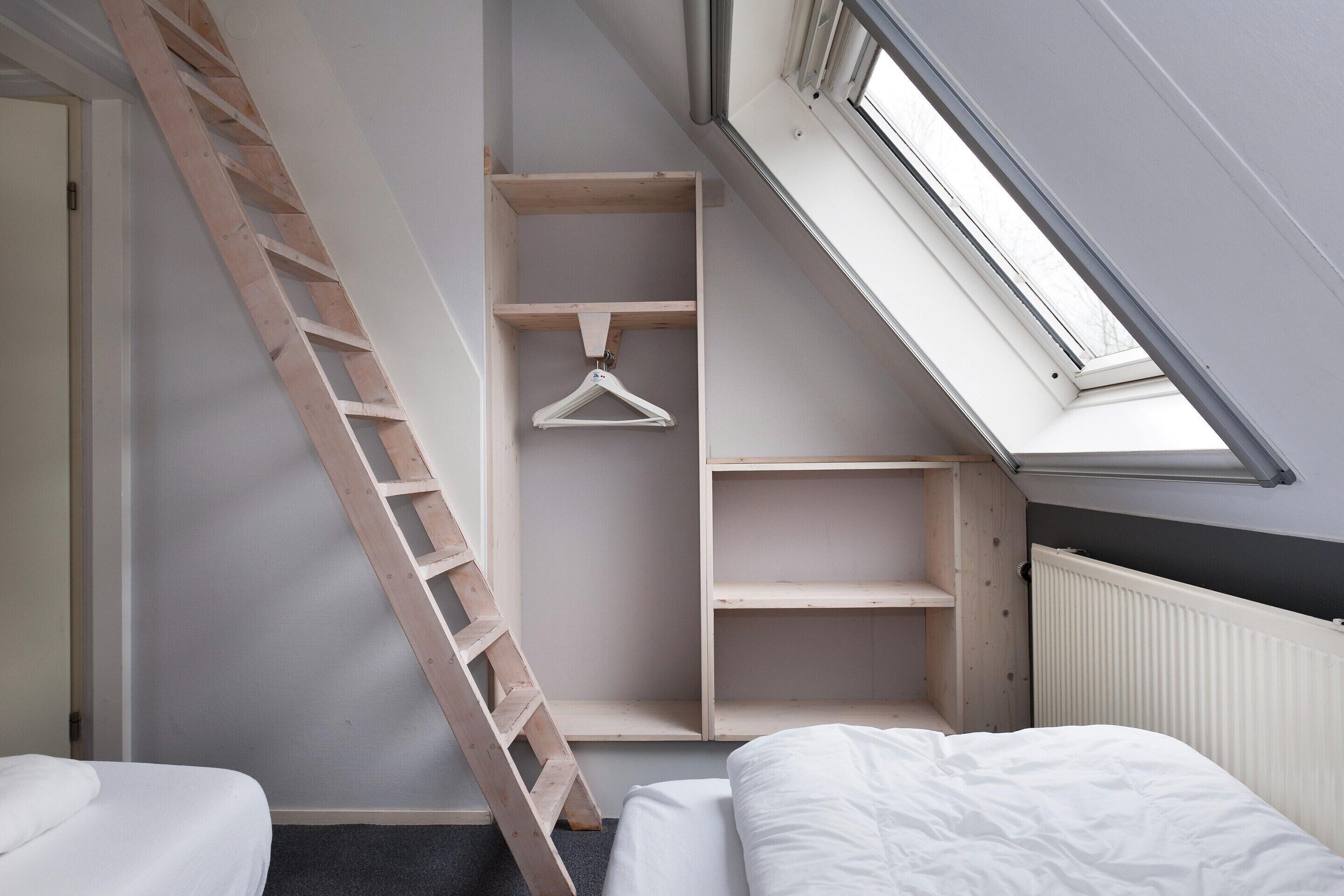 Un dormitorio con tragaluz, escalera de madera y estanterías empotradas.