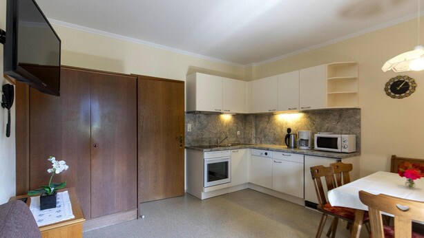 A compact kitchen with a microwave, oven, and sink, wooden cabinets, and a dining area with a table and chairs. - Holiday Flats in St. Georgen am Kreischberg (Sankt Georgen am Kreischberg)