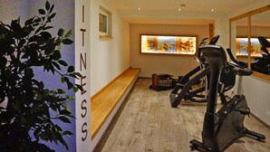 Een fitnessruimte met trainingsapparatuur, een bank en een kunstwerk aan de muur.