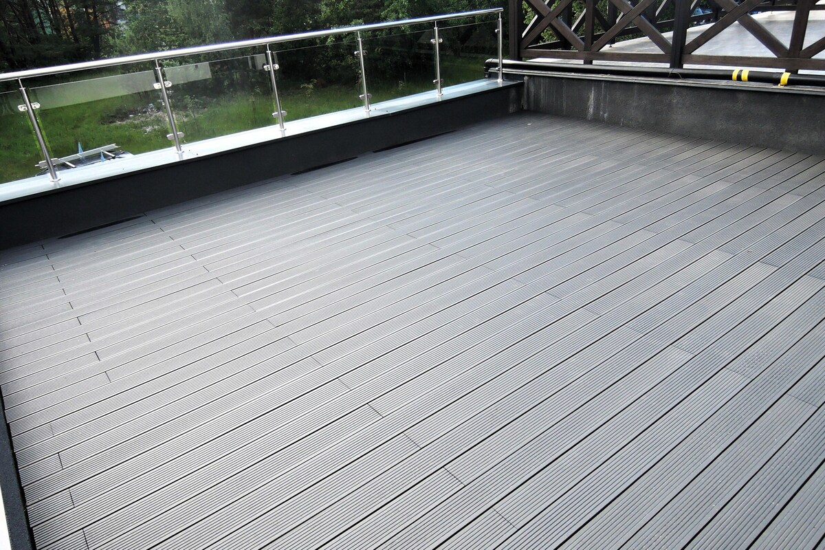 A wooden deck with a glass railing overlooking a grassy area.