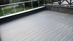 Een houten terras met glazen hekwerk met uitzicht op een gazon.
