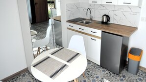 Een compacte keuken met witte kastjes, een roestvrijstalen spoelbak en een koffiezetapparaat. Er staat een rond tafel met een placemat en een prullenbak ernaast.