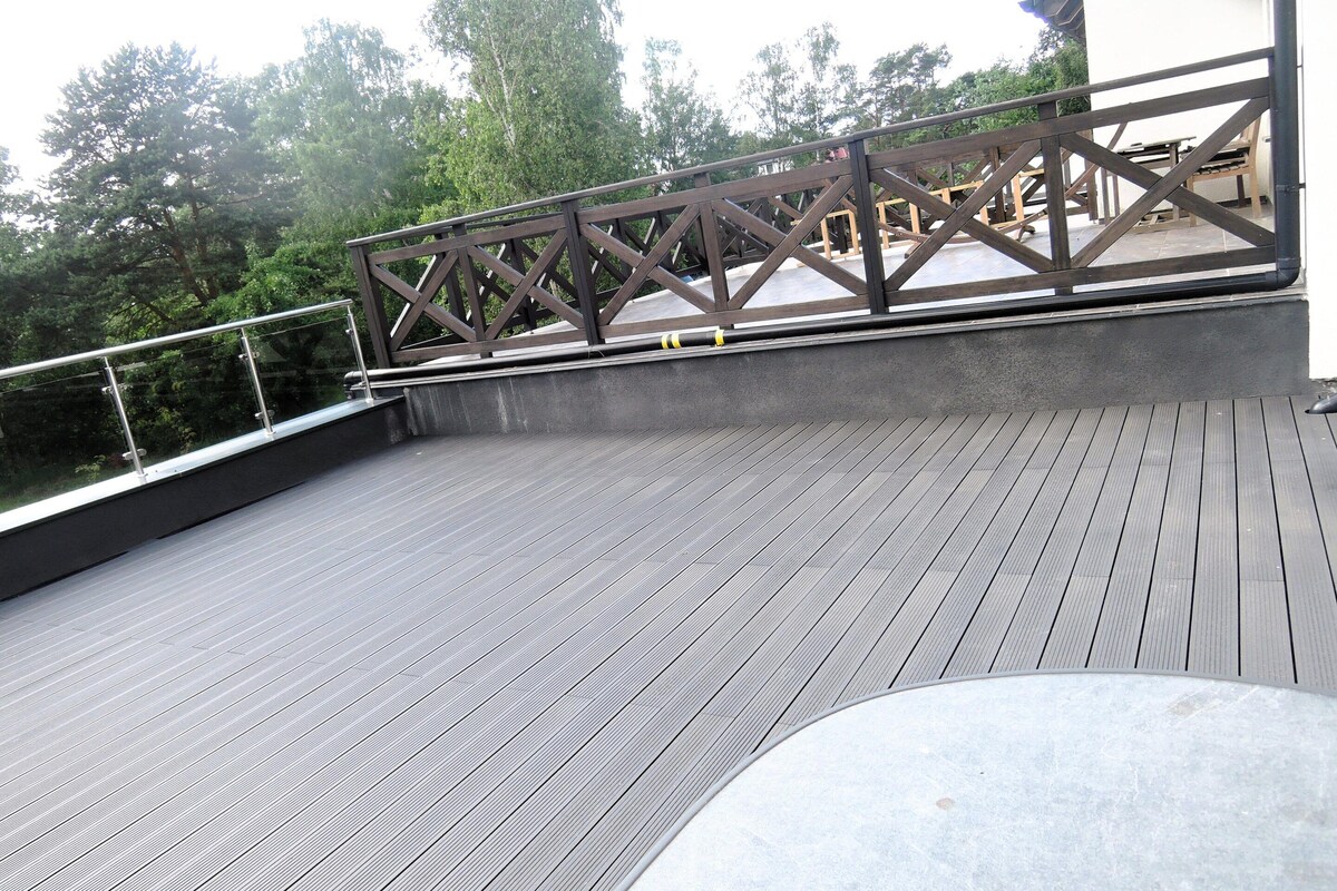 A rooftop deck with a wooden railing, a concrete floor, and a view of trees in the background.