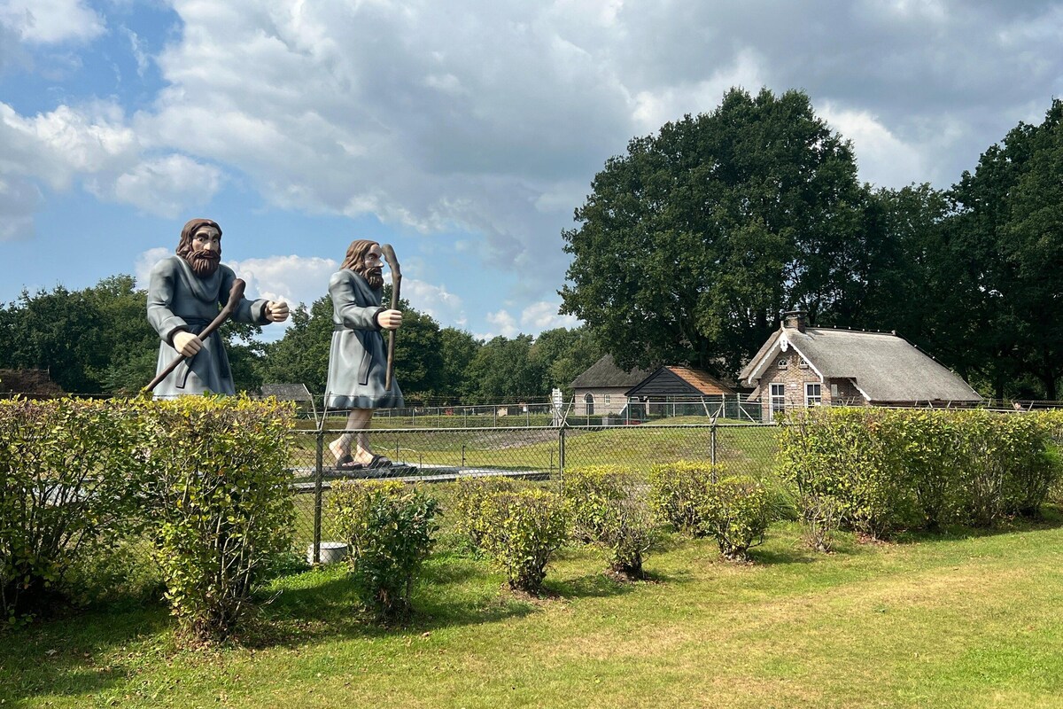 Deux statues dans un parc, avec une maison et des arbres en arrière-plan.