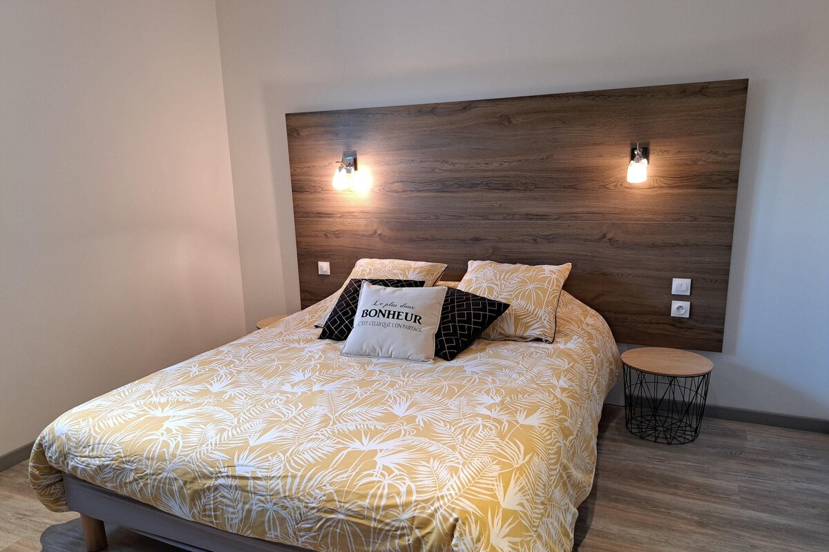 A neatly made bed with a patterned bedspread, two wall-mounted light fixtures, and a small round side table.