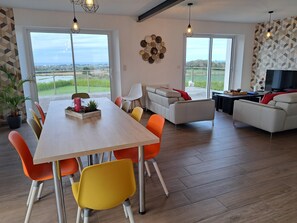 A modern living room with a sofa, dining table, and chairs, large windows with a view, and a TV. - Holiday Home 10 Pers., Panoramic sea View, Cleder (Cleder)