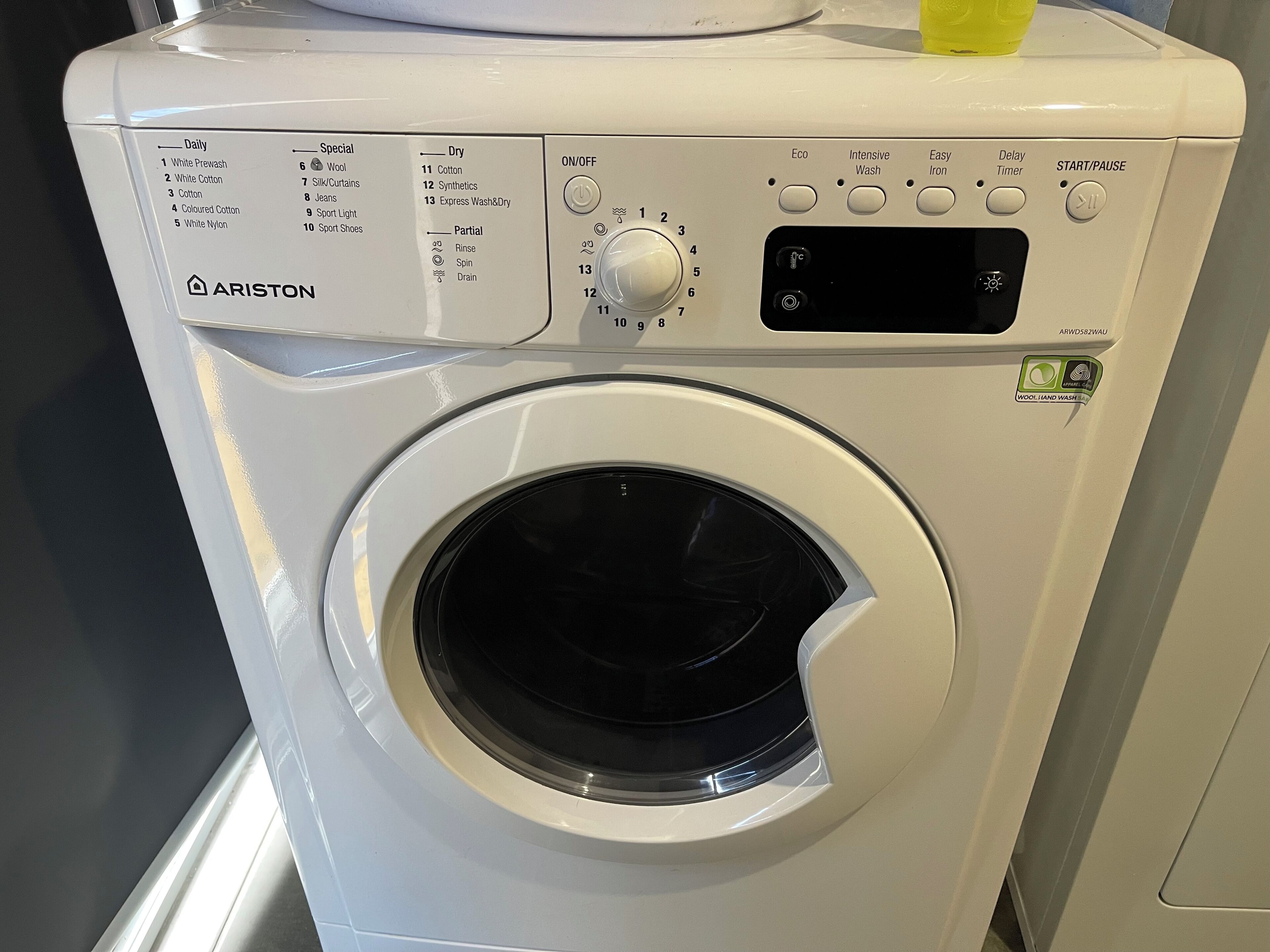 A front view of a white Ariston washing machine with a control panel, including buttons for various wash cycles and settings.
