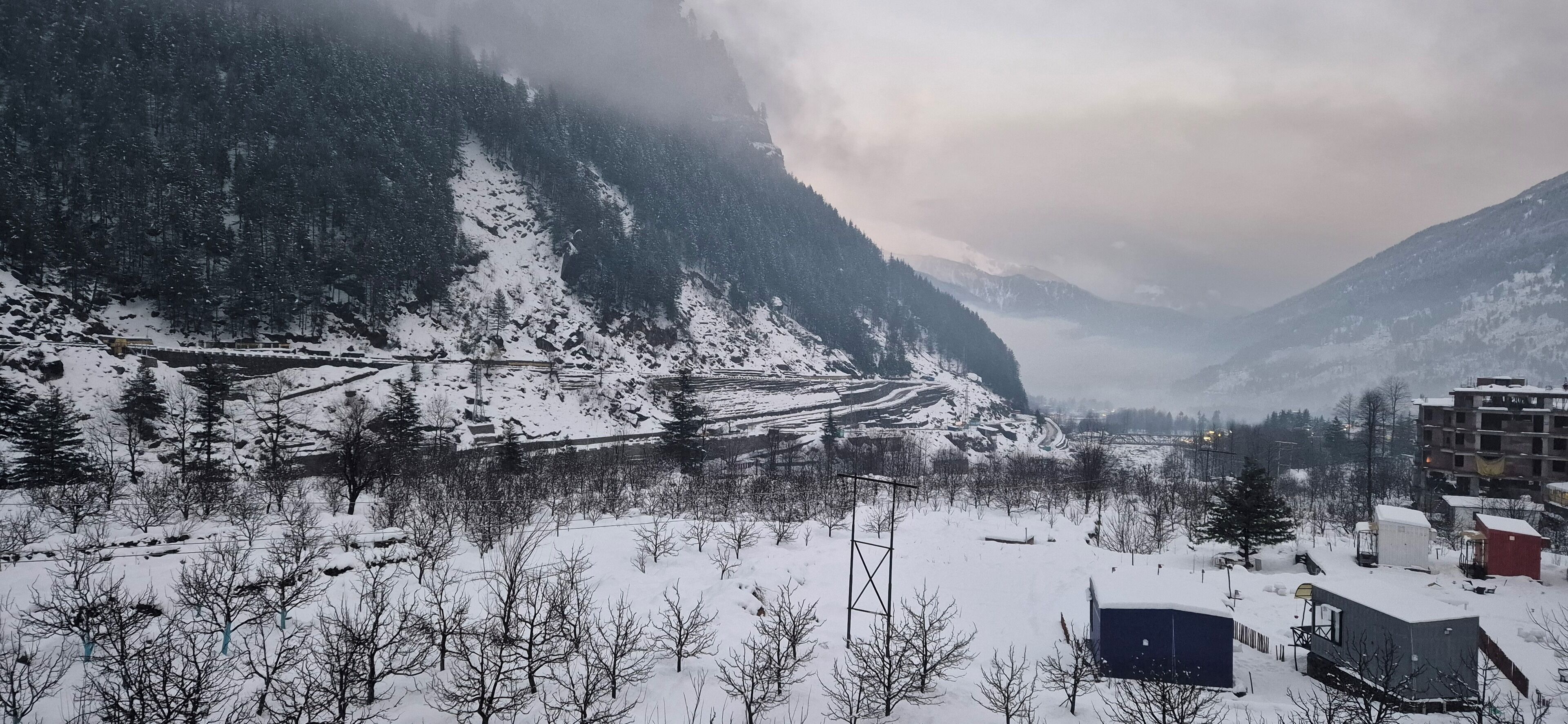 A snowy mountain landscape with a road, buildings, and trees.