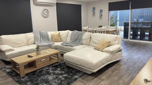 Moderni olohuone, jossa on kulmasohva, sohvapöytä ja ruokailutila, jossa on pöytä ja tuolit.