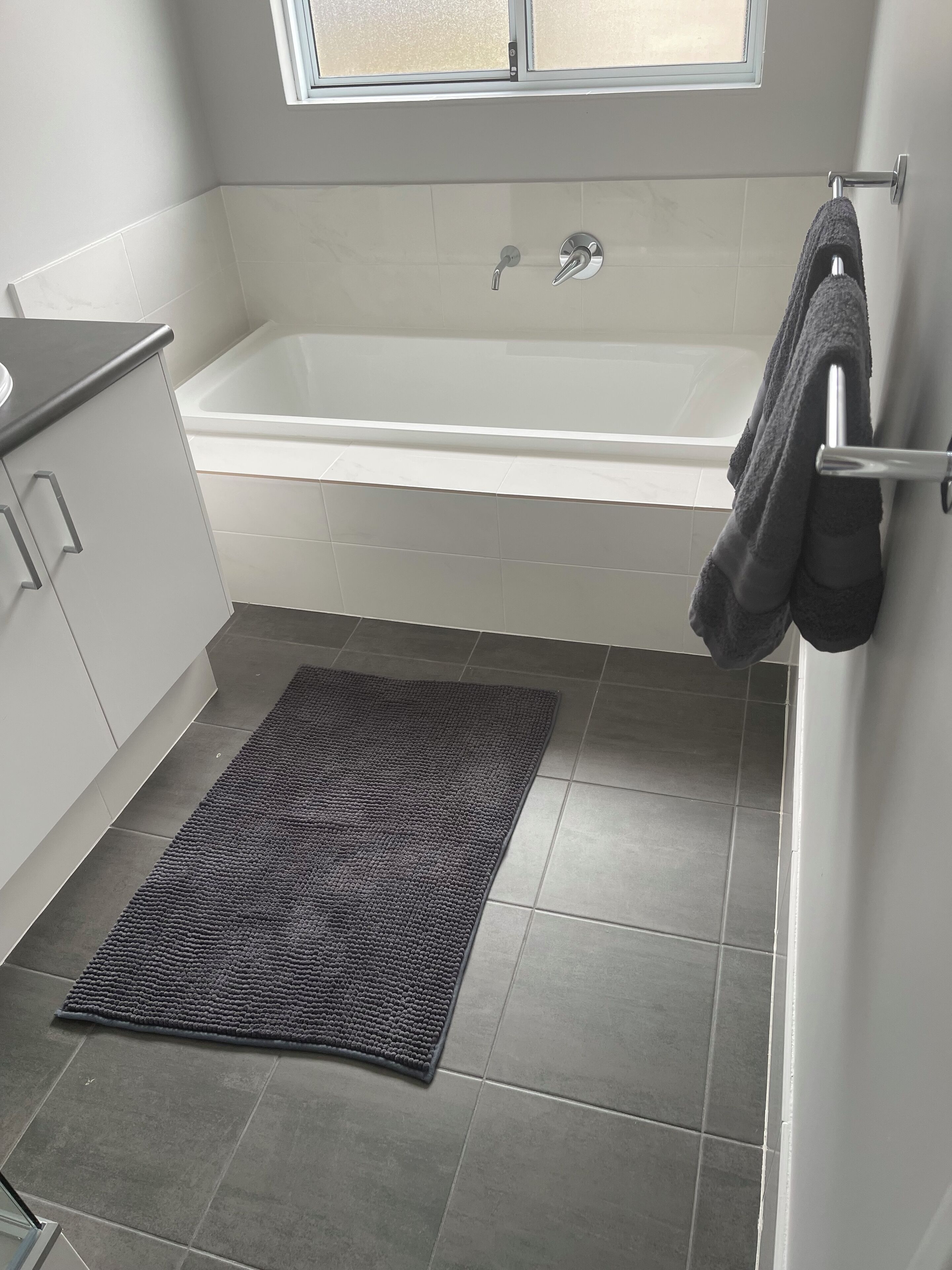 A modern bathroom with a bathtub, a towel rack, and a dark gray rug.