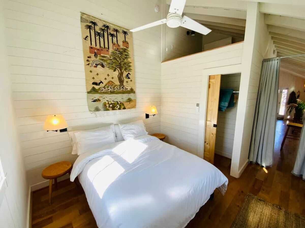 Un dormitorio con cama, dos mesitas de noche, ventilador de techo y una lámpara de pared.