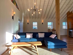 A spacious living area with a large blue sectional sofa, a wooden coffee table, and a modern chandelier. - Aftonshire Cottage - Heart of Afton's Wine Region (Afton)