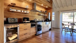 A modern kitchen with wooden cabinetry, stainless steel appliances, and a dining area with a table and chairs. - Aftonshire Cottage - Heart of Afton's Wine Region (Afton)