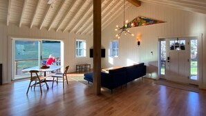A spacious interior with a high ceiling, wooden beams, a large dining table, blue sofa, and large windows. - Aftonshire Cottage - Heart of Afton's Wine Region (Afton)
