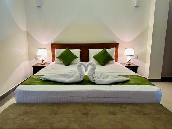 A hotel room with a large bed, two nightstands, green pillows, and a decorative swan towel arrangement.