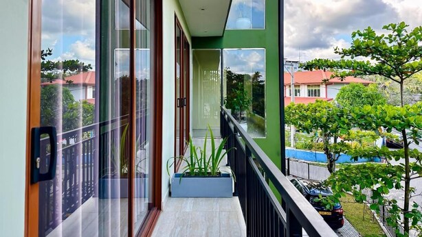 A balcony with large glass doors, a potted plant, and a view of buildings and trees. - Located in Galle, 2.5 km from  Beach, Fortwill City Hotel provide accommodation  (Galle)
