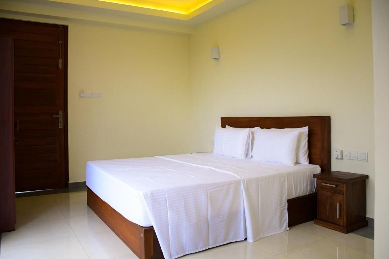 A neatly made bed with white linens in a room with cream walls and a wooden door.