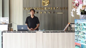A reception desk at Vang Vieng River Resort Hotel with a laptop, a sign instructing to inform the receptionist if customers want their room cleaned, and a decorative orchid arrangement. - Vang Vieng Rivercube Hotel (Vang Vieng)