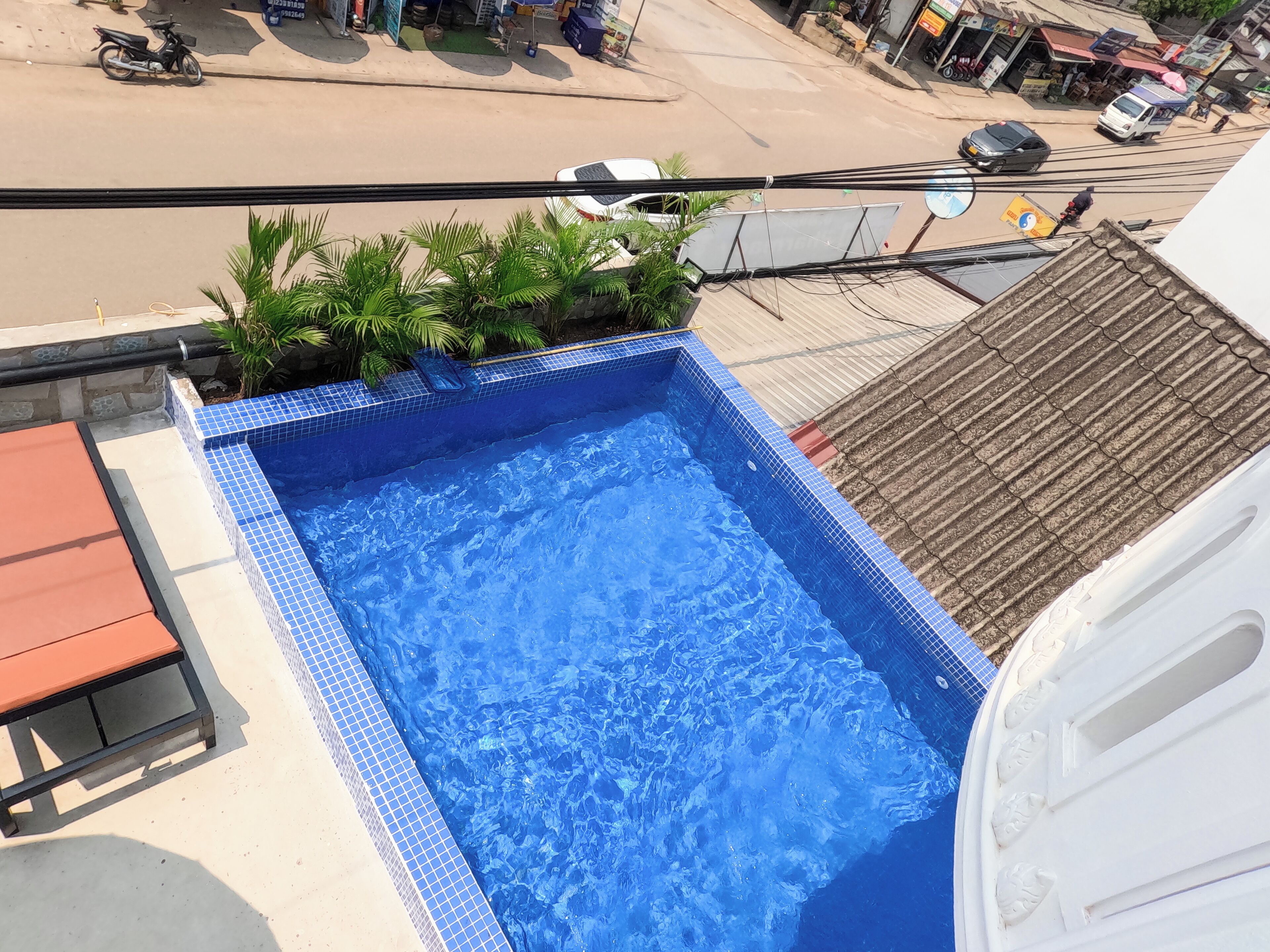 A rooftop swimming pool with blue tiles, a red bench, and a view of the street below.