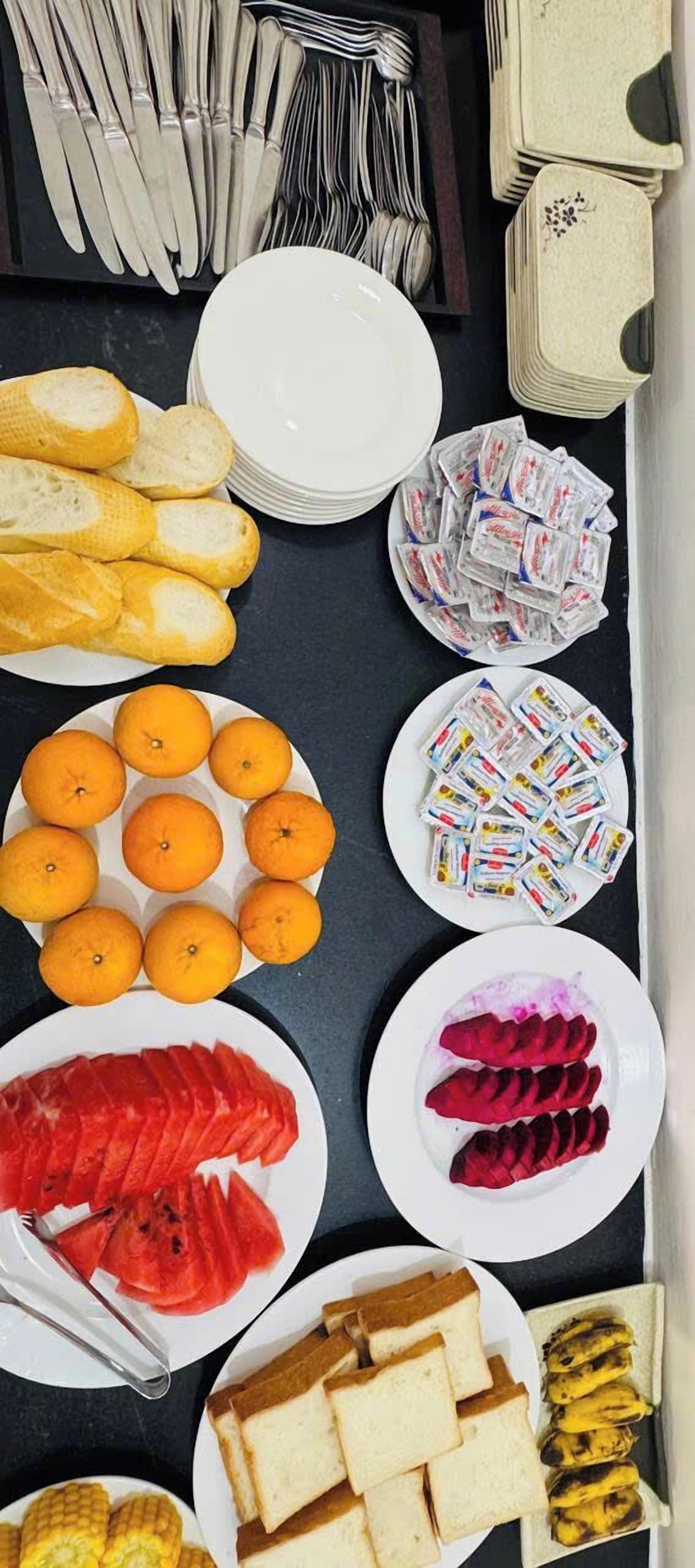 Una mesa con platos de pan, naranjas, sandía y otros alimentos.