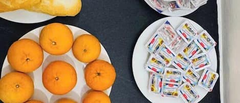 Una mesa con platos de pan, naranjas, sandía y otros alimentos.