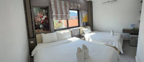 A hotel room with two beds, a small desk, and a window with a view of the outside.