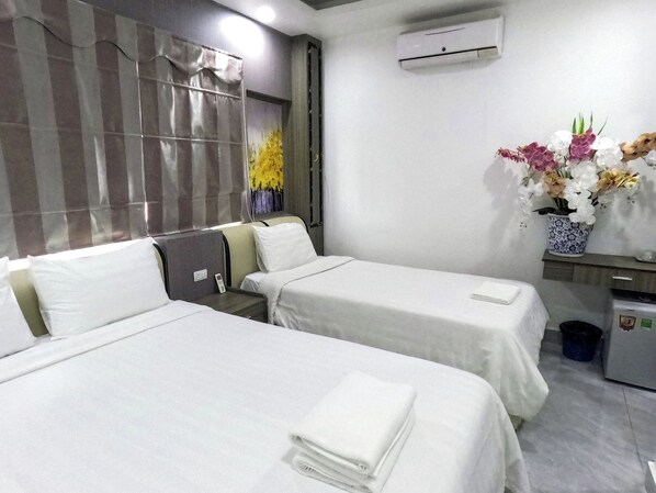 A hotel room with two beds, a small desk, a trash bin, and a wall-mounted air conditioner.
