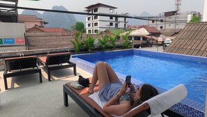 A poolside area with lounge chairs, a tiled pool, and a view of surrounding buildings. - Vang Vieng Rivercube Hotel (Vang Vieng)