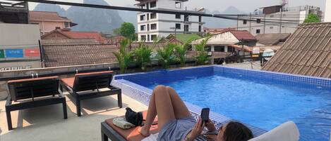 A poolside area with lounge chairs, a tiled pool, and a view of surrounding buildings.