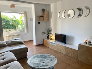 Un salon moderne avec un canapé, un téléviseur posé sur une console en bois, une table ronde et une fenêtre avec des rideaux.