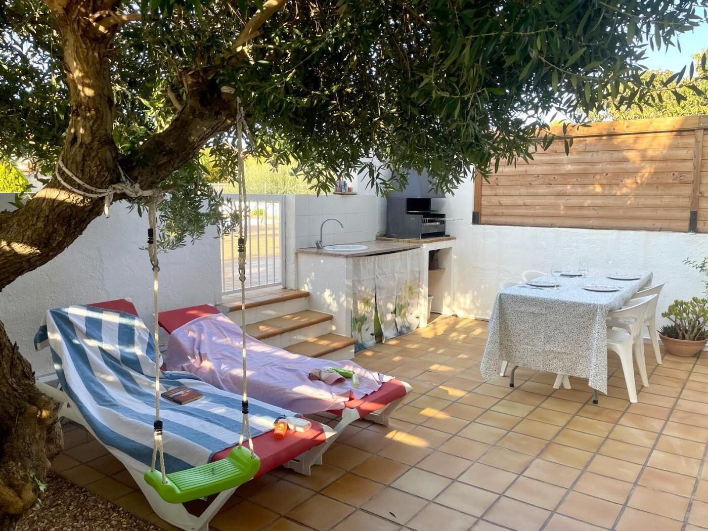 A patio with a swing chair, a small table with chairs, a kitchen area, and a bed.