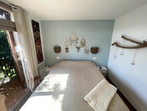 Een slaapkamer met een groot bed, een raam en wanddecoraties, waaronder dromenvangers.