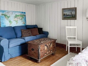 A room with a blue sofa, a white chair, a wooden chest, a world map on the wall, and a framed picture.
