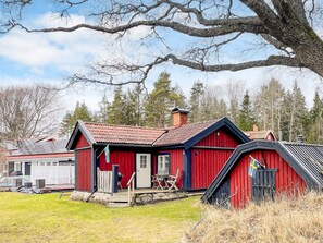A red barn with a porch and a chimney, surrounded by a grassy yard and trees.