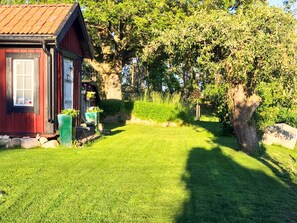 A red wooden cabin with a window and a door, surrounded by a well-maintained lawn and trees.