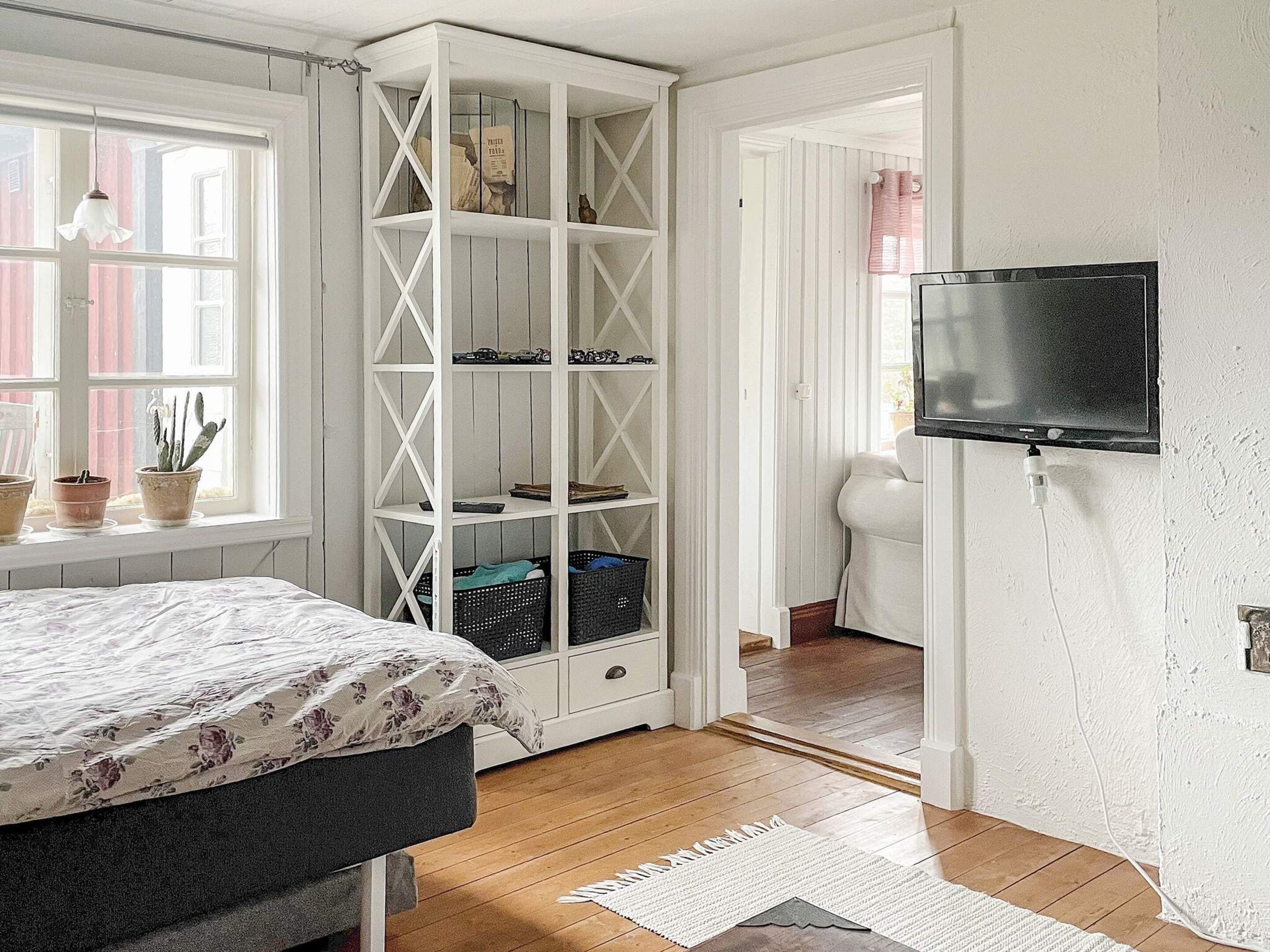 Un dormitorio con cama, un armario blanco, televisor y una ventana con cortinas.