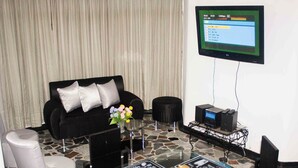 A modern living room with a black sofa, a glass coffee table with placemats, a flat-screen TV mounted on the wall, and a small side table with electronic devices. - Cozy apartment in downtown Pereira (Pereira)