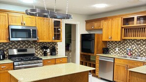 A modern kitchen with wooden cabinets, a central island with stools, stainless steel appliances, and a tiled backsplash. - Waterfront 3BR 2BA Home near Galveston, Kemah, NASA, NRG, Rodeo, Houston (La Porte)