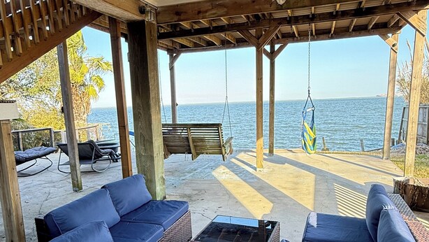 A covered outdoor seating area with wicker furniture and a swing chair, overlooking a body of water. - Waterfront 3BR 2BA Home near Galveston, Kemah, NASA, NRG, Rodeo, Houston (La Porte)